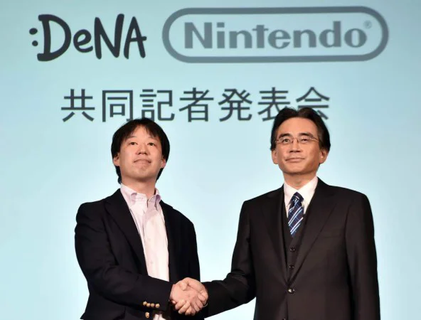 Japan's video game giant Nintendo president Satoru Iwata (R) shakes hands with Japanese online game operator DeNA president Isao Moriyasu during a press conference in Tokyo on March 17, 2015. Nintendo said on March 17 it was teaming up with a mobile gaming company to develop games for smartphones in what could be a turning point for the Japanese giant which has long refused to enter the soaring market.  AFP PHOTO / Yoshikazu TSUNO        (Photo credit should read YOSHIKAZU TSUNO/AFP/Getty Images)